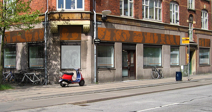 Facaden på Ungerådgivningen Amager Øst Københavns Kommune med flot dekorativt skilt i perforeret corten stål. Perforeringen danner et mønster som viser close up af ansigterne på de forskellige brugere ar rådgivningsbutikken.