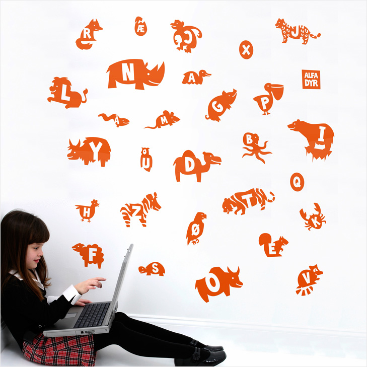 Girl sitting omn the floor with laptop next to wall with orange wallstickers with different animals. The animals have the first letter in their name on them.
